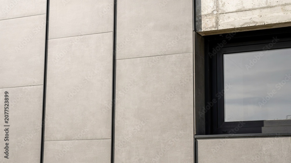 Fototapeta premium Wall cladding tiles made of light grey ceramic material surround a modern window frame in a minimalist building design.