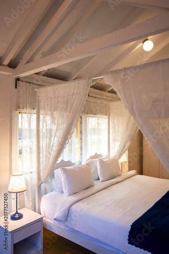 Obraz na płótnie Close-up of a white canopy bed with pillows and bedside lamps in a white-themed cottage bedroom, showcasing elegant furnishings and a clean, contemporary interior