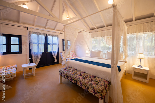 фотографія White-themed cottage house interior featuring a canopy bed with bedside lamps, a bed bench, and a sofa, showcasing a bright, elegant, and contemporary bedroom with a clean aesthetic