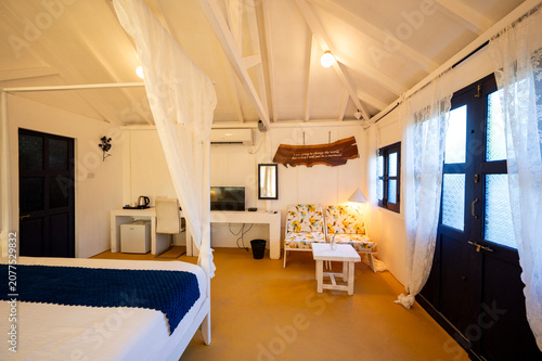 Bild auf Leinwand White-themed cottage house interior featuring a canopy bed with bedside lamps, a bed bench, sofa, and TV, showcasing a bright, elegant, and contemporary bedroom with a clean aesthetic
