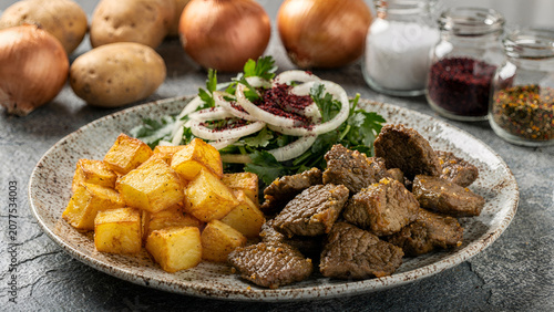Close up of a traditional Turkish meat dish with roasted potato cubes and sumac onion salad on a ceramic plate
