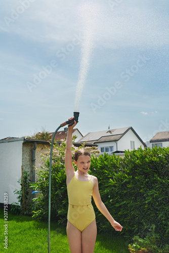 A cheerful child plays with water sprinklers in the garden during the summer. Creatively watering the garden—with fun and high spirits. An authentic, real little girl.