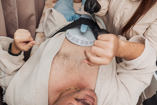 Konstfotografi Middle-aged Hispanic man undergoing Emsculpt HIFEM body contouring treatment as an esthetician secures the abdominal applicator for non-invasive muscle strengthening and body sculpting
