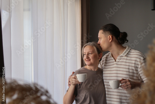 Canvas-taulu Loving mid-age man kisses woman, while couple enjoying coffee by the window, sharing a quiet connection and peaceful domestic routine