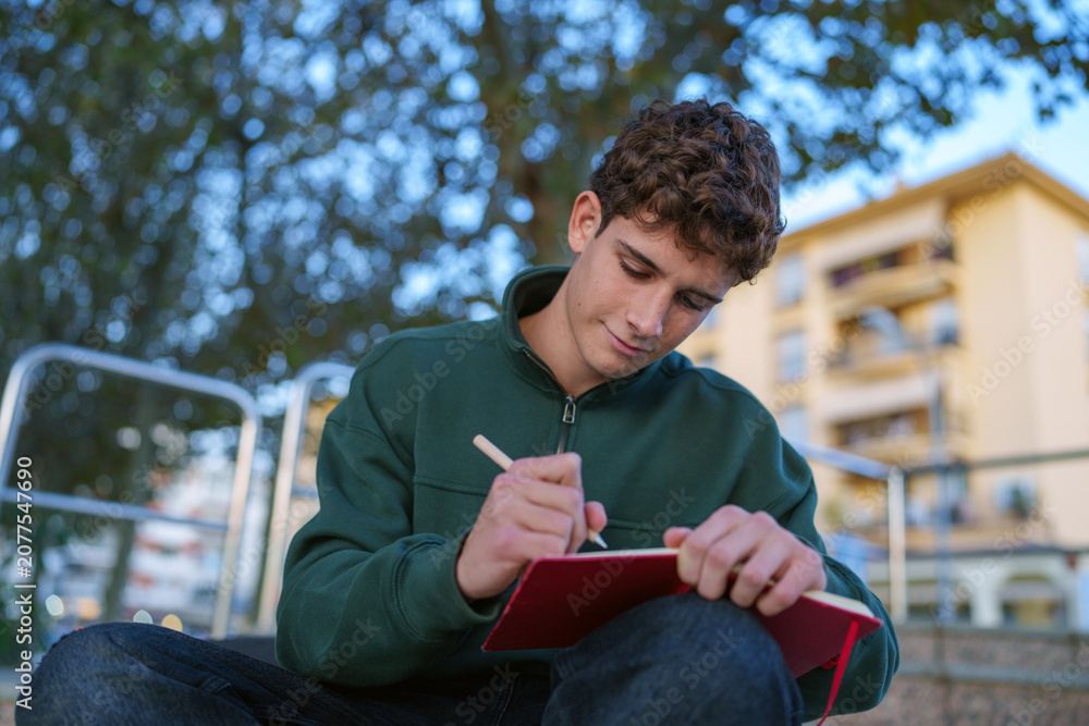 Obraz premium Young student writing in red notebook outdoors, concentrating on studying or creating a new idea