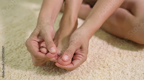 Close-up of a person holding and massaging a painful toe while sitting on the floor. Concept of foot pain, toe injury, gout, bunion, inflammation, podiatry, and foot care.