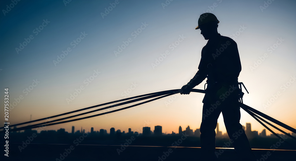Fototapeta premium Construction worker silhouette against city skyline at sunset