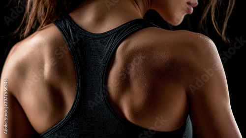 Extreme close up , back muscle of sport woman wearing black tank top , blakc background.