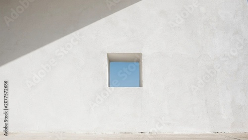 Square window cut into a minimalist white concrete wall creates a geometric composition with dramatic morning shadows.