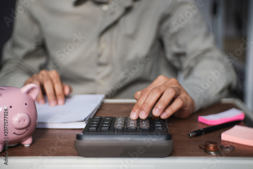 person uses calculator and writes a financial report, recording income expenses savings and deductions to manage costs and maintain an accurate budget balance.