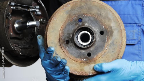 Auto mechanic in blue gloves and overalls holds a brake drum, repairing the car's brake system.