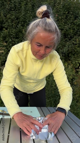 Senior female tourist wrapping apples in metallic foil sheet for baking on charcoal grill outdoors.