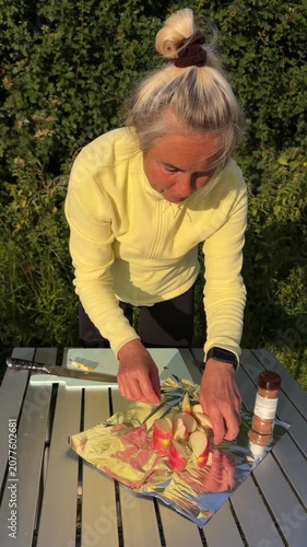 Senior woman arranging sliced organic apples on aluminum foil preparing a healthy outdoor dessert.