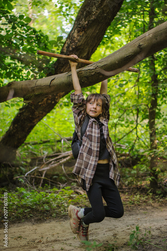 Cheerful kid with backpack hanging on tree in forest 