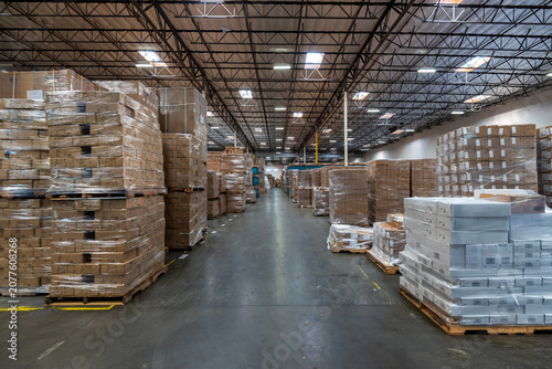 Interior of a spacious and modern logistics warehouse with large quantities of cardboard boxes stacked on pallets for storage.