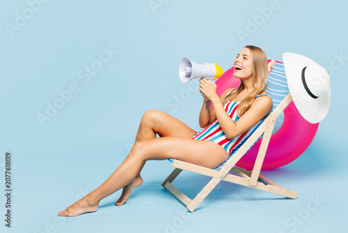 Full body young beautiful sexy woman wear bikini swimsuit rest near hotel pool lies on deckchair scream in megaphone about sale isolated on plain blue background. Summer vacation sea sun tan concept.