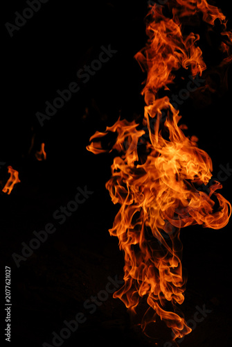 Close-up of vivid orange flames forming dynamic swirling patterns against a black background. The fluid movement and dramatic glow create an abstract composition. 
