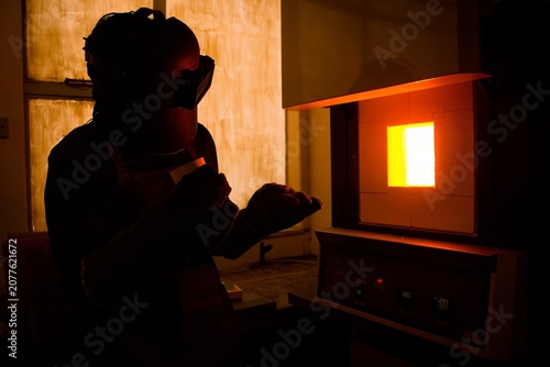 A researcher opening a high temperature muffle furnace during pyrometallurgical research in a laboratory setting with glowing orange light