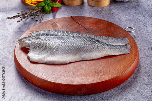 Raw sea bass fillets on round wooden cutting board with fresh herbs