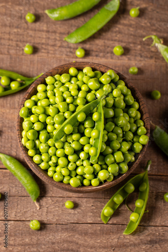 Fresh green peas and pods in a bowl on wooden table. Vegetable healthy food.  