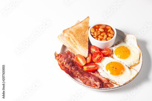 Delicious traditional English breakfast with fried eggs, beans, bacon, tomatoes and toasts