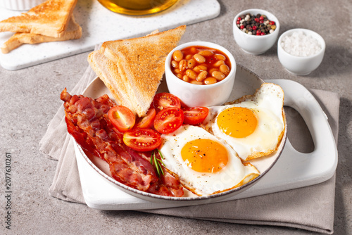 Delicious traditional English breakfast with fried eggs, beans, bacon, tomatoes and toasts