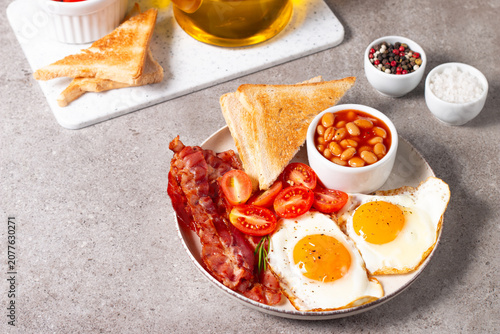 Delicious traditional English breakfast with fried eggs, beans, bacon, tomatoes and toasts