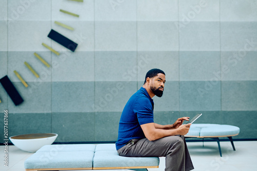 Billede på lærred Confident businessman sitting on a bench, using a digital tablet
