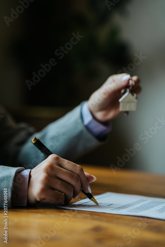 Real estate agent holding a house key with a model home, symbolizing homeownership and property purchase.