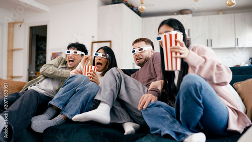 Obraz na płótnie Friends sitting on a couch wearing 3D glasses, eating popcorn, and reacting to a