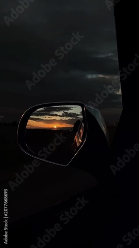 Car side mirror reflecting sunset with dark clouds in background  