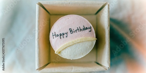 Miniature bento cake in a craft paper box, minimalist pastel frosting with a simple handwritten 'Happy Birthday' message, aesthetic soft focus, top-down view.
