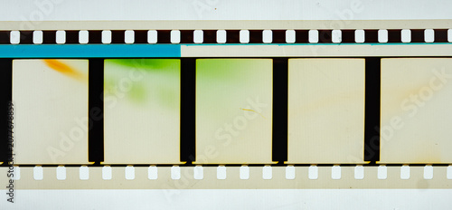 Long horizontal vintage 35mm motion picture film strip featuring blank frames and classic sprocket holes. Authentic analog cinema celluloid isolated on white with green light leaks and blue stripe