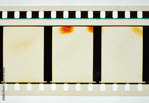 Vintage 35mm motion picture film strip featuring blank frames and classic sprocket holes. Authentic analog cinema celluloid isolated on white with orange light leak burn marks