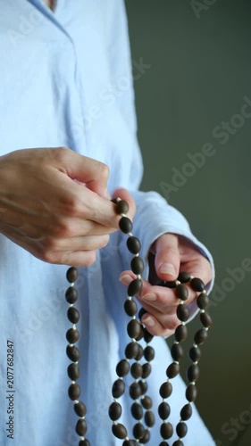 Female hands holding wooden prayer beads, mindfully counting them during spiritual practice of meditation or prayer for concentration, faith, and inner peace in serene setting. Vertical video.