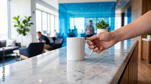 Tableau sur toile Close-up of a female hand holding a white coffee mug on a marble counter in a modern, brightly lit office space