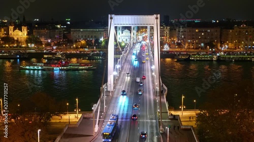 High angle view of the illuminated Erzsebet Bridge in Budapest at night with flowing car traffic, river cruises on the Danube, and glowing city lights under a dark sky