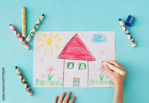 Konstfotografi Child drawing a colorful house with crayons on paper over a blue background