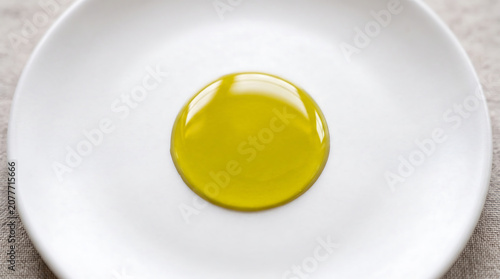 Macro shot of a single drop of golden olive oil glistening on a clean white plate with soft natural light highlighting its smooth texture and vibrant color