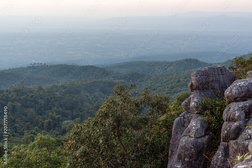 Fototapeta premium Lan Hin Taek Viewpoint in Phu Hin Rong Kla National Park, Thailand. Panoramic view of green forested mountains under cloudy sky. Unique stone formations in the foreground.