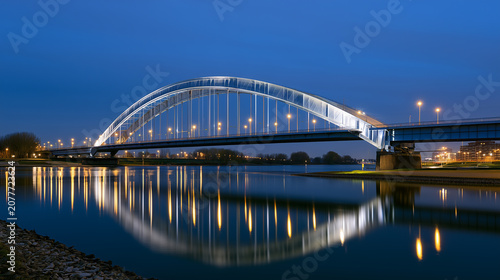 Illuminated arch bridge reflecting on calm river at blue hour cityscape with night lights	
