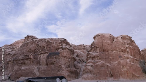 A scenic view of weathered sandstone rock formations and cliffs at the Little Petra archaeological site in Jordan under a cloudy sky.