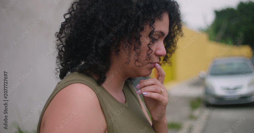 Obraz premium Worried woman standing outdoors with hand on chest, mid-profile view, urban street background, showing preoccupation and struggling with inner turmoil, emotional depth visible