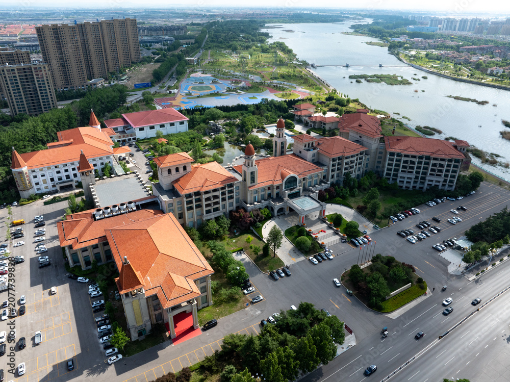 Fototapeta premium Aerial view of red-roofed architectural complex along river in Shouguang with wetlands and greenery