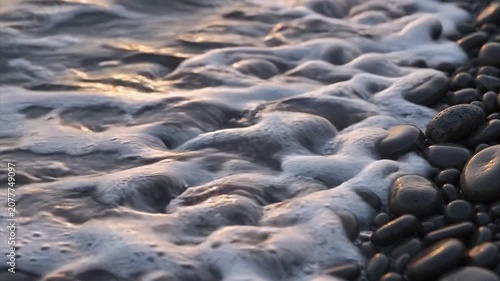 Gentle Ocean Waves Washing Over Smooth Black Pebbles at Sunset