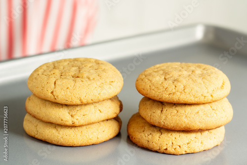 Freshly baked homemade peanut butter cookies stacked on a metal baking sheet with a soft kitchen background.