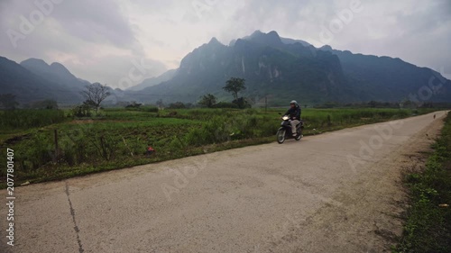 Motorbike rider stopping on scenic rural road in Vietnam with majestic mountain landscape, man on scooter driving rural road for tourism