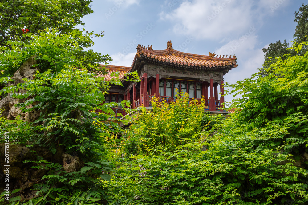 Fototapeta premium Traditional Imperial Palace Pavilion Rising Above Lush Greenery and Scholar's Rocks at Daytime in the Forbidden City, Beijing, China