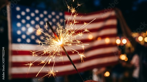 Burning sparkler in front of a blurred american flag at night