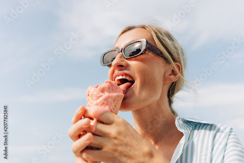Woman enjoying a melting pink ice cream cone on a sunny day wearing sunglasses and a striped shirt